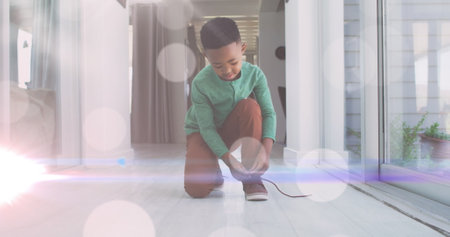 Image of lights over happy african boy tying shoe. childhood, independence, spending time at home concept digitally generated image.の写真素材