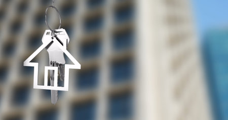 House-shaped keychain image over blurred high-rise building background. Real estate, home ownership, property, investment, modern, urbanの写真素材