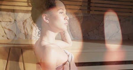 Image of candle and light spots over biracial woman relaxing in sauna. Self care, beauty, relaxation, wellbeing and lifestyle, digitally generated image.の写真素材