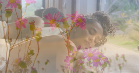 Image of pink flowers in garden over biracial woman lying on massage table. Nature, self care, beauty, relaxation, wellbeing and lifestyle, digitally generated image.の写真素材