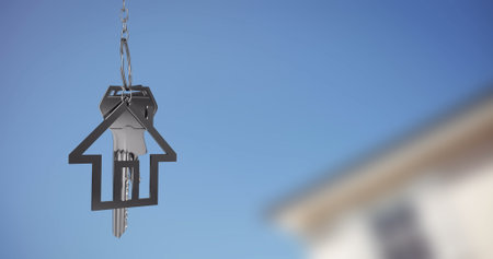 House-shaped keychain with keys image over blurred building and blue sky background. Real estate, property, home, ownership, security, metalの写真素材