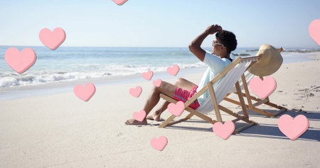 Image of pink hearts over african american man relaxing on beach. Summer, vacation, lifestyle and digital interface concept digitally generated image.の写真素材