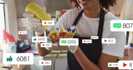 Image of media icons over african american woman preparing hotdog. social media and communication...