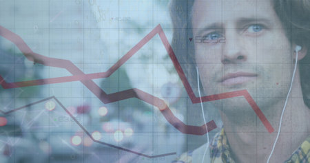 Caucasian male partner looking at declining graph. He has light stubble, brown hair, and is wearing earphonesの写真素材