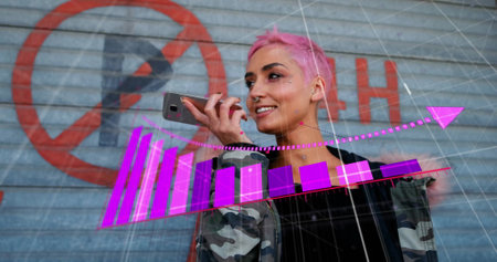 Image of arrow on falling graphs over biracial woman talking on speaker of cellphone. Digital composite, multiple exposure, communication, loss, reduction, report, business and technology concept.の写真素材