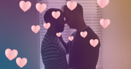 Image of heart icons over diverse gay couple embracing. pride month and celebration concept digitally generated image.の写真素材