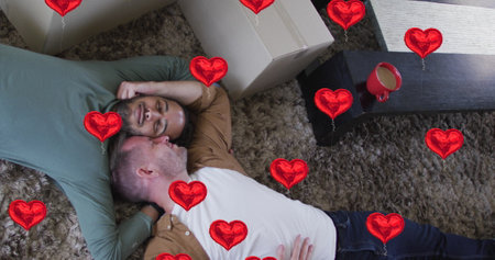 Image of heart icons over diverse gay couple lying. pride month and celebration concept digitally generated image.の写真素材