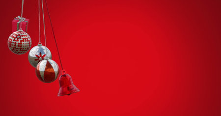Image of gift box, bell and baubles swinging against red background. Digitally generated, hologram, illustration, decoration, christmas, holiday, event, winter and celebration concept.の写真素材