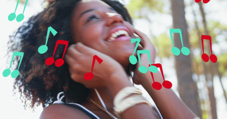 Image of notes icons over smiling african american woman with earphones dancing. dance day and celebration concept digitally generated image.の写真素材