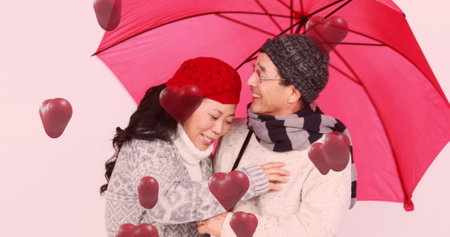Image of red hearts over couple in love with pink umbrella. Valentine's day, love and romance concept digitally generated image.の写真素材
