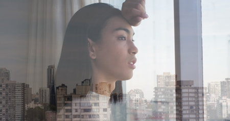 Image of cityscape over biracial woman looking through window. Lifestyle, fashion and light concept digitally generated image.の写真素材