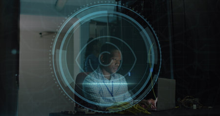 Image of eye retina scanner over african american male engineer using laptop at server room. Cyber...