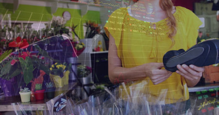 The female florist is using a credit card terminal in the flower shop. The stock market display shows red, blue, purple, and green stock market tickers and graphs. The prices are going up and down.の写真素材