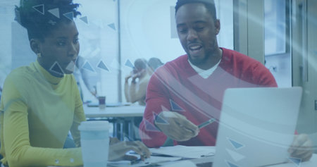 Two african american business colleagues are talking and using a laptop in their office. They are...