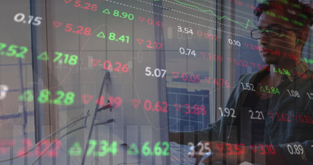 Image of graph and trading board over tired biracial man working over laptop in office. Digital...