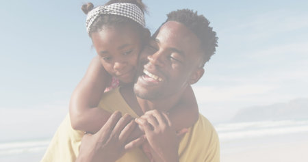 African American father holding young daughter, both smiling at beach. He has short black hair, she wears headband; both in casual clothesの写真素材