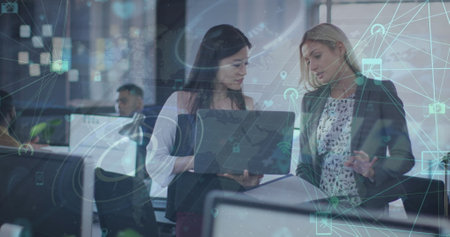 Image of globes of digital icons over two diverse women discussing over a laptop at office. Global...