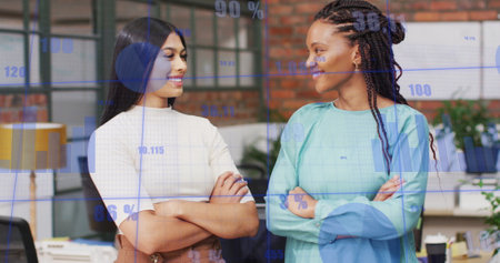 Image of graphs and changing numbers over smiling diverse female coworkers standing arms crossed. Digital composite, multiple exposure, report, growth, close up and business concept.の写真素材