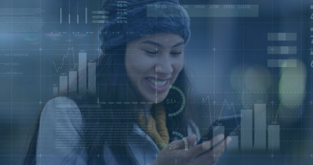 Young biracial professional wearing hat is looking at a smartphone. She has long black hair, a warm...