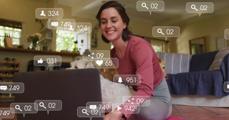 Digital icons on speech bubbles against caucasian woman sitting with her dog using laptop at home. national pet month awareness conceptの写真素材
