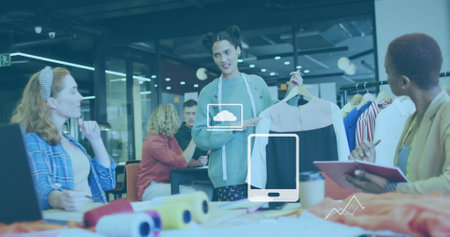 Image of application icons and graphs over diverse designer showing garment to coworkers. Digital composite, cloud computing, infographic technology, fashion, creative, teamwork and office.の写真素材