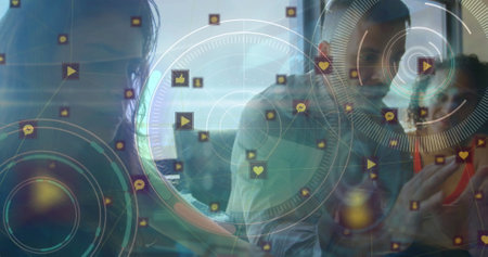 Image of circles with social media and computer icons over colleagues discussing in office. Hologram, digital composite, multiple exposure, business, teamwork, internet and technology concept.の写真素材