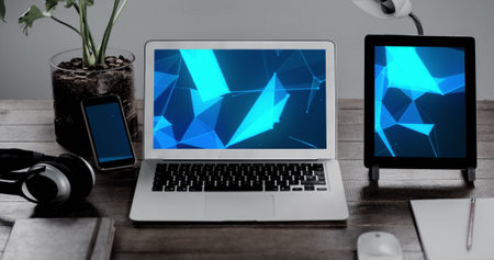 Image of technological devices with blue shapes on screen on desk. Global technology, abstract background and digital interface concept digitally generated image.の写真素材