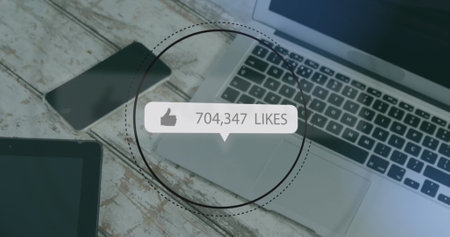 Image of like icon with increasing numbers over digital tablet, diary, laptop on wooden surface. Computer interface and business data technology conceptの写真素材