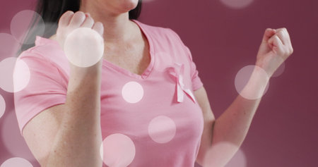Image of light spots over caucasian woman with pink ribbon on pink background. Breast cancer awareness concept digitally generated image.の写真素材