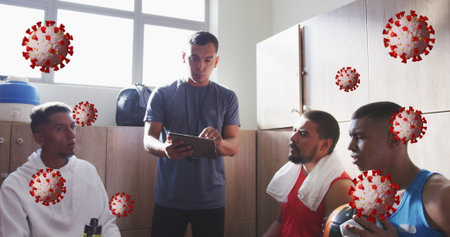 Image of covid-19 cells over male coach discussing with male soccer players in locker room. Covid-19...