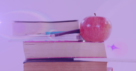 Image of glowing light over apple on stack of books. international literacy day and reading concept digitally generated image.の写真素材