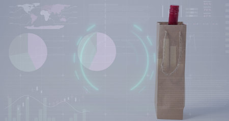 In this image, a wine bottle is seen in a shopping bag against a white background. An image of a circle is seen over a digital screen with financial graphs and data. This image is a representation of the global finance, economy, and technology concept.の写真素材