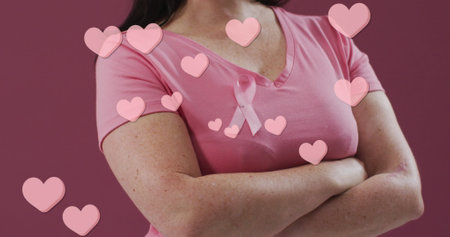Image of hearts text over caucasian woman with pink ribbon on pink background. Breast cancer awareness concept digitally generated image.の写真素材