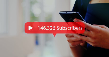 Caucasian woman holding smartphone, showing subscriber count. She has long brown hair, wearing blue...
