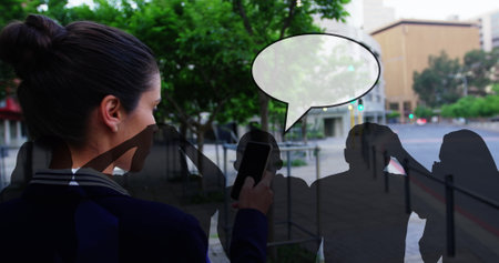 Caucasian colleague holding smartphone, looking at screen. She has brown hair in bun, wearing a dark jacketの写真素材