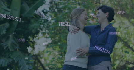 Image of social media icons over caucasian lesbian couple hugging each other in the park. Social media networking technology and lgbt relationship conceptの写真素材