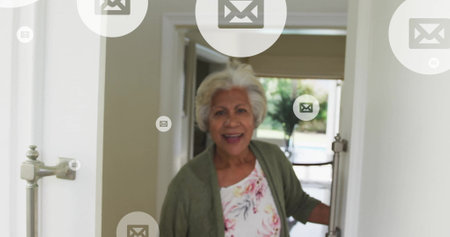 Image of envelope icon in circles over senior smiling biracial woman opening door. Digital...
