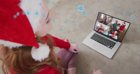 Image of snow over happy caucasian woman in santa hat on laptop image call with her family....