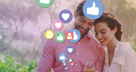 Image of media icons over happy biracial couple using smartphone. social media and communication interface concept digitally generated image.の写真素材