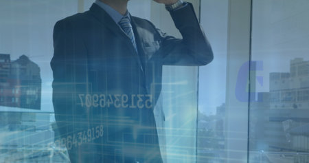Caucasian male colleague wearing suit standing by window. He has short brown hair, looking at smartphone with reflection on glassの写真素材
