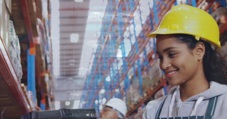 Hispanic female coworker wearing yellow hard hat is scanning items. She has dark hair, a warm smile, and is in a warehouseの写真素材