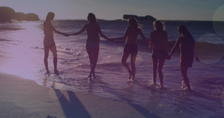 Image of glowing lights over group of female friends by the sea. Friendship, summer and holiday...