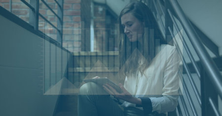 Image of graphs over thoughtful caucasian woman sitting on staircase using digital tablet. Digital...