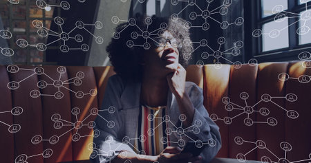 Biracial young professional sitting on sofa, thinking deeply. She has curly black hair, wears a...