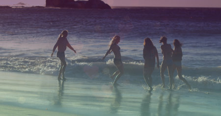 Image of glowing lights over group of female friends by the sea. Friendship, summer and holiday concept digitally generated image.の写真素材