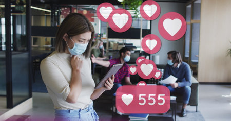 Image of media icons over diverse business people wearing face masks and using tablet. global...