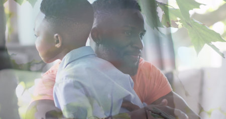 Image of leaves over happy african american father and son hugging on sofa. family, togetherness, spending quality time concept digitally generated image.の写真素材