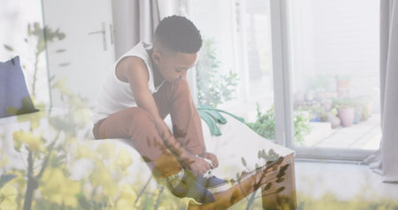 Image of plants over african american boy tying shoe on bed. childhood, independence, spending time at home concept digitally generated image.の写真素材