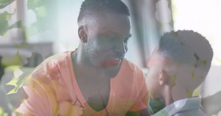 Image of leaves over happy african american father and son hugging on sofa. family, togetherness, spending quality time concept digitally generated image.の写真素材
