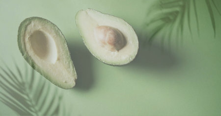 Image of palm tree leaves over halved avocado on green background. Fruit, healthy diet and vegan...